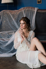 Beautiful bride in white lace lingerie, with bare shoulder sitting in a hotel room. Happy wedding morning.