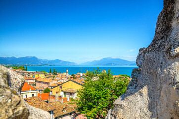 Fototapeta na wymiar View of historical centre Desenzano del Garda old town, lake and mountain range through merlons of brick stone ruined wall of medieval castle, blue sky copy space, Lombardy, Northern Italy