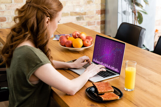 Side view of woman using laptop with charts near toasts and orange juice on table - Powered by Adobe