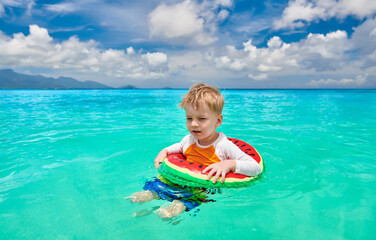 Toddler boy on beach swimming with inflatable ring