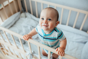 Little cute adorable boy
 is in the nursery with a white crib and laughs