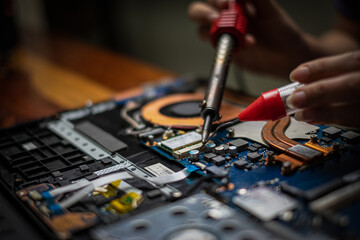 Close-up hand technician repairing broken laptop notebook computer with electric soldering Iron