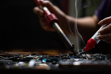 Close-up hand technician repairing broken laptop notebook computer with electric soldering Iron