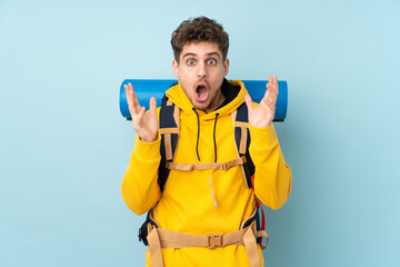 Young mountaineer man with a big backpack isolated on blue  background with surprise facial expression