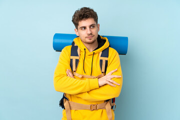 Young mountaineer man with a big backpack isolated on blue  background thinking an idea
