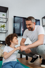 happy father bumping fists with smiling son at home