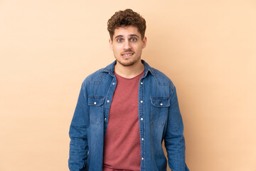 Fototapeta premium Caucasian man isolated on beige background having doubts and with confuse face expression