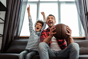 excited kid and father holding basketball while watching championship