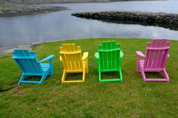 Multi coloured wooden chairs on grass near water