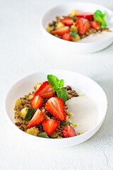 Homemade crunchy granola with nuts, dried fruits, fresh strawberries, mint and yogurt (fermented baked milk) on a white plate. Healthy breakfast concept.