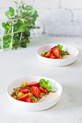 Homemade crunchy granola with nuts, dried fruits, fresh strawberries, mint and yogurt (fermented baked milk) on a white plate. Healthy breakfast concept.