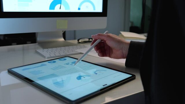 Pretty business woman working on tablet computer and analyzing a marketing report in her office on white desk using a pen
