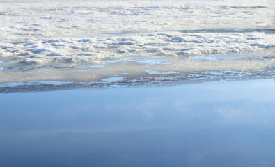 Melting of ice and snow on the lake in spring. Snow and ice in the reservoir. Reflection of the sky in the lake. Selective focus. Landscape