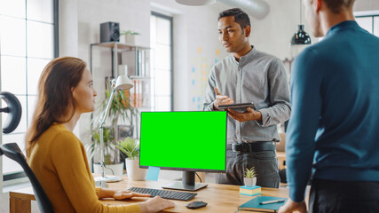 Three Start-up Entrepreneurs Work on Desktop Computer with Green Mock-up Screen, They Discuss...