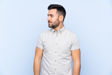 Fototapeta premium Young handsome man with beard over isolated blue background looking side