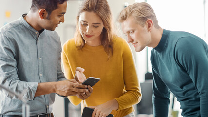 In the Office: Three Diverse Start-up Entrepreneurs Have Meeting and Discussion about the Project. Share Touch Screen Digital Tablet and Smartphone Screens.Young Professionals Smile and Joke Around.