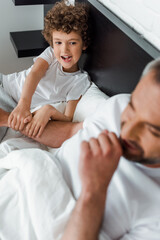 Fototapeta premium selective focus of curly kid looking at happy father in bedroom