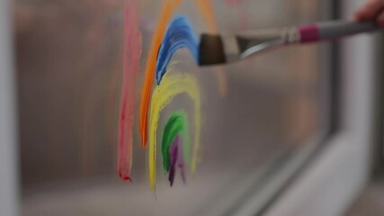 Self-isolation at home. Child quarantined girl paints a rainbow on a glass window. Art Therapy and Distance Learning	