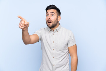 Young handsome man with beard over isolated blue background pointing away