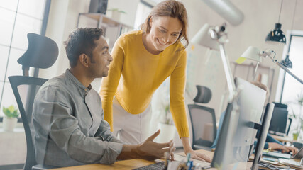 Handsome Indian Professional Sitting at His Desk Working on Laptop Computer, Young Beautiful Team Leader Gives Advice about Project Details. Office with Young Professionals Work. Dutch Angle.