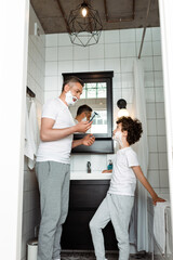Obraz premium handsome father with shaving foam on face holding razor near curly son