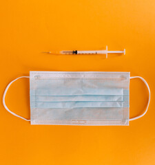 Top view of medical concept with syringe and mask on orange background for coronavirus prevention. Covid-19 kit. Copy Space
