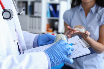 Close-up of professional doctor holding breast implant. Nurse in uniform. Qualified medical worker with patient history in hands and red stethoscope. Modern medicine concept