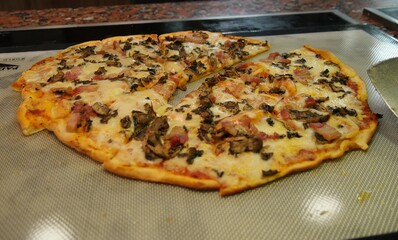 Thin-crust pizza slices with bacon bits and mushrooms heating up on the grill