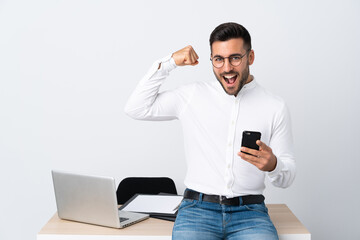 Young businessman holding a mobile phone making strong gesture