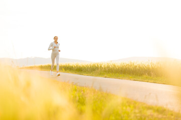 Sportliche junge Frau joggt abends zwischen Feldern