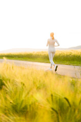 Fototapeta na wymiar Sportliche junge Frau joggt abends zwischen Feldern