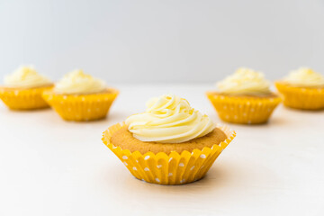Five lemon cupcakes with vanilla frosting and yellow spotty cases.  Focus on centre front cupcake with other arranged behind out of focus against a light background