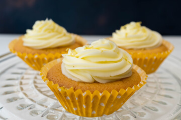 Close up of three cupcakes with frosting sitting on a glass dish with a dark background