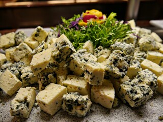 Cubes of blue cheese served on a board decorated with greens