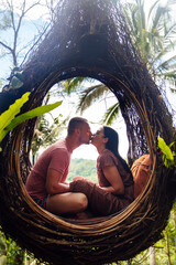 A tourist couple sitting on a large bird nest on a tree at Bali island