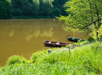 two old wooden rowing boat with lush spring grass on the river Berounka bank in spring with trees, countryside in golden afternoon light