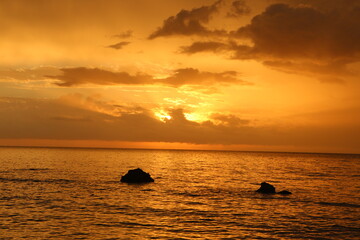 Fototapeta na wymiar contrasty panorama seascape shot of a rocky beach at low tide with a golden orange sunset with beautiful sky reflection on ocean water surface. Koh Lanta, Thailand