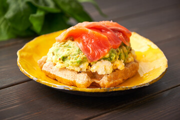 Belgian waffle with scrambled egg, avocado and salmon on wood table. Plate, bacon. Keto Breakfast variation.