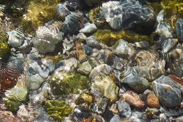 View of colorful sea pebbles by the seashore through clear transparent flowing sea water.