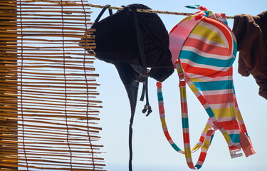 Colorful striped bikini hanging out to dry on a washing line in summer next to a reed curtain.