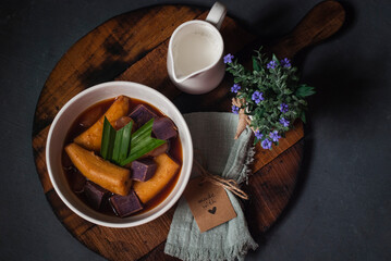 Banana kolak with sweet potato & sugar palm fruits addition on dark grey background. Kolak is an Indonesian dessert based on palm sugar,coconut milk & pandanus leaf. Very popular dish on Ramadan iftar