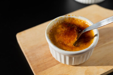 Homemade creme brulee in white ramekin  with sugar burn top up cracking with spoon on black background with copy space. French dessert creme brulee