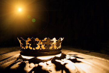 The crown on a black background is illuminated by a golden beam. Low-key image of a beautiful queen...