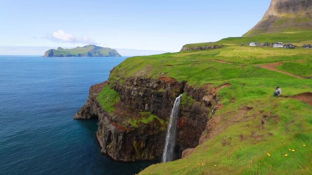 Photogtapher takes picture of Mulafossur Waterfall. Sunny summer view of Gasadalur village, Vagar, Faroe Islands, Denmark, Europe. Full HD video (High Definition).
