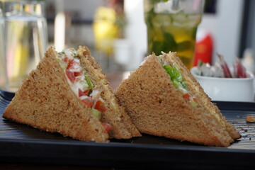 Two club sandwiches placed on a black plate at a restaurant. Close-up photo of a club sandwich. Sandwich with prosciutto, vegetables, lettuce and mayo on a fresh sliced rye bread on wooden background.