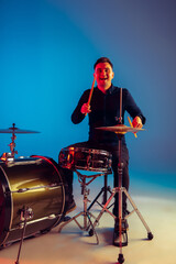 Caucasian male drummer improvising isolated on blue studio background in neon light. Performing,...