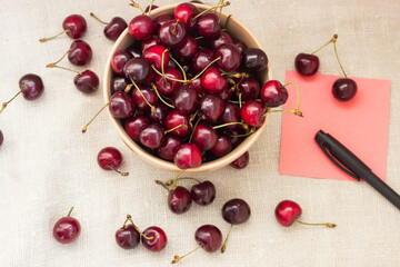 ripe cherries in a plate on a wooden background and paper for notes