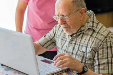 Senior man and his caregiver with laptop at home spending time togheter