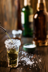 An alcoholic drink at the bar counter is poured into a tequila glass with salt at the edges, in the...