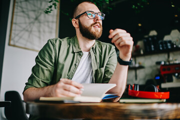 Handsome creative author sitting at cafe interior with notebook